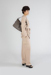 Beige jumpsuit med bälte i midjan, stora cargofickor och avslappnad passform. Svart handväska med vävt mönster, bärs på axeln.