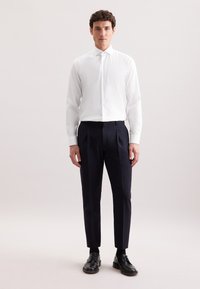 Camicia a righe verticali bianche abbinata a pantaloni azzurri sartoriali, con vestibilità slim, maniche lunghe e scarpe nere con lacci.