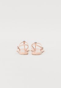 Sandales en plastique rose avec une semelle plate, dotées de fines brides et d'un accent de boucle métallique. Texture lisse et design minimaliste.