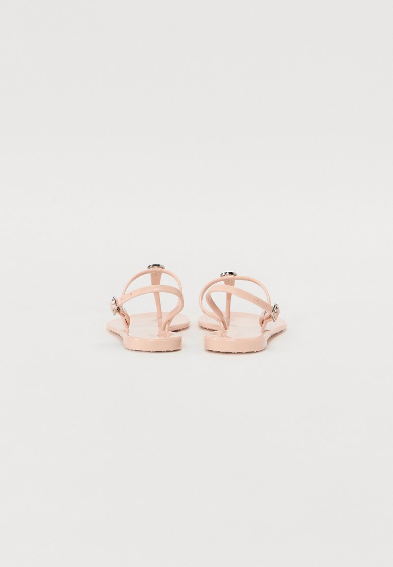 Sandales en plastique rose avec une semelle plate, dotées de fines brides et d'un accent de boucle métallique. Texture lisse et design minimaliste.
