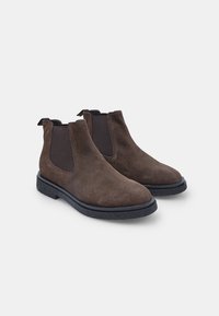 Stivaletti in suede marrone con pannelli elastici laterali, punta arrotondata e suola nera testurizzata. Due linguette sul tallone per indossarli facilmente.