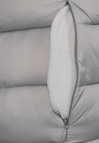 Sezione di giacca a vento grigia con tasca con zip, caratterizzata da un tessuto esterno liscio e un morbido rivestimento soffice visibile all'interno della tasca.