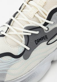 White mesh sneaker featuring a textured gray overlay, black accents, light blue detailing, and cream laces with a prominent "Camper" logo.