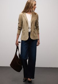 Blazer de pana beige con cuello de solapa con muesca, combinado con jeans de pierna ancha azul oscuro y un bolso de hombro de ante marrón. Bailarinas negras de punta puntiaguda.