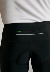 Schwarze Radshorts mit einer Reißverschlusstasche auf der Rückseite, die grüne Akzente aufweist. Enthält ein gepolstertes Design für Komfort und reflektierende Details.