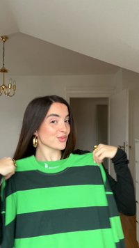 T-shirt listrado em verde e preto com gola redonda, feito de tecido. A camisa apresenta largas listas horizontais e um corte relaxado.
