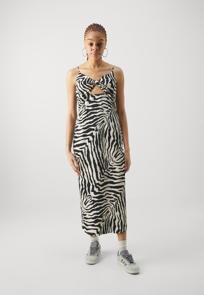 Zebra raksts midi kleita ar pagriešanas mezglu dizainu melnā un krēmkrāsā. Spageti siksniņas un gluda auduma, kombinācijā ar pelēkajām sporta apaviem.