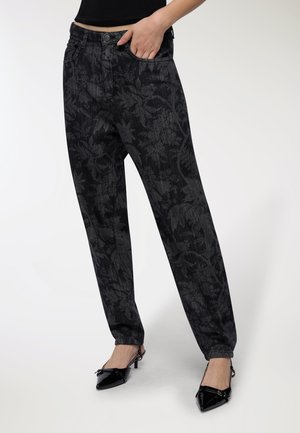 Pantaloni in denim nero con un motivo floreale, caratterizzati da una vestibilità rilassata, tasche frontali e chiusura con bottone, abbinati a scarpe nere a punta.