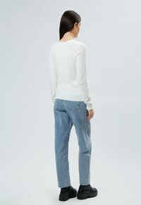 Maglione bianco e soffice con maniche lunghe, design aderente, abbinato a jeans azzurri a vita alta e stivali neri con zeppa.