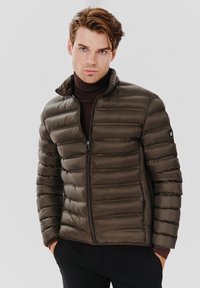 Kurtka puchowa w ciemnooliwkowym kolorze, pikowana konstrukcja z poziomymi szwami, pełny zamek błyskawiczny, kołnierz stójkowy oraz czarny detal z logo na rękawie.