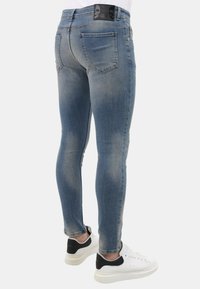 Slim-fit, lichtblauwe denim jeans met een vervaagd uiterlijk, vijf-pocket ontwerp en zwart label op de tailleband. Gecombineerd met wit- en zwartgekleurde sneakers.