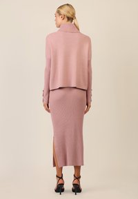 Rosa Strickpullover und gerippter Rock mit einem seitlichen Schlitz, beide verfügen über eine weiche Textur und eine lässige Passform. Schwarze Riemchenabsätze runden den Look ab.