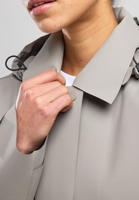 Light gray waterproof jacket with a structured collar, buttons, and an elastic loop near the neck for adjustment. Smooth, matte finish.