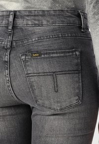 Le jean en denim noir présente deux poches arrière avec un design de couture distinctif et une petite étiquette "Lois" en fil doré sur la poche droite.