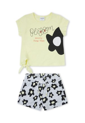 Top amarillo de manga corta con motivo floral en blanco y negro y texto "bloom Groovy Floral Vibes", combinado con pantalones cortos blancos cubiertos de flores negras.