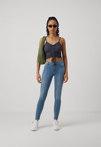 Top corto navy con detalle de fruncido, combinado con jeans ajustados azul claro y zapatillas blancas. La modelo lleva un bolso de hombro acolchado verde.
