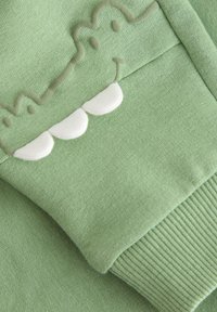 Φούτερ από ανοιχτό πράσινο ύφασμα με σχέδιο βατράχου, διαθέτει υφασμένη ραφή, λευκές λεπτομέρειες στα δόντια και ριμπ μανσέτες.