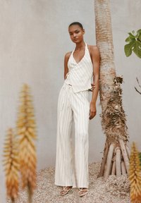 Top halter bianco con righe verticali e vita annodata, abbinato a pantaloni a palazzo. Il tessuto testurizzato e il dettaglio annodato arricchiscono il design.