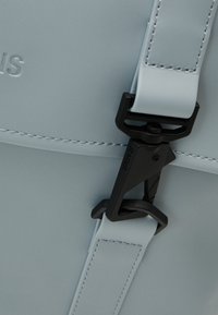 Sac en cuir bleu clair avec fermeture à clip en plastique noir et surpiqûres visibles sur les sangles et le bord du rabat.