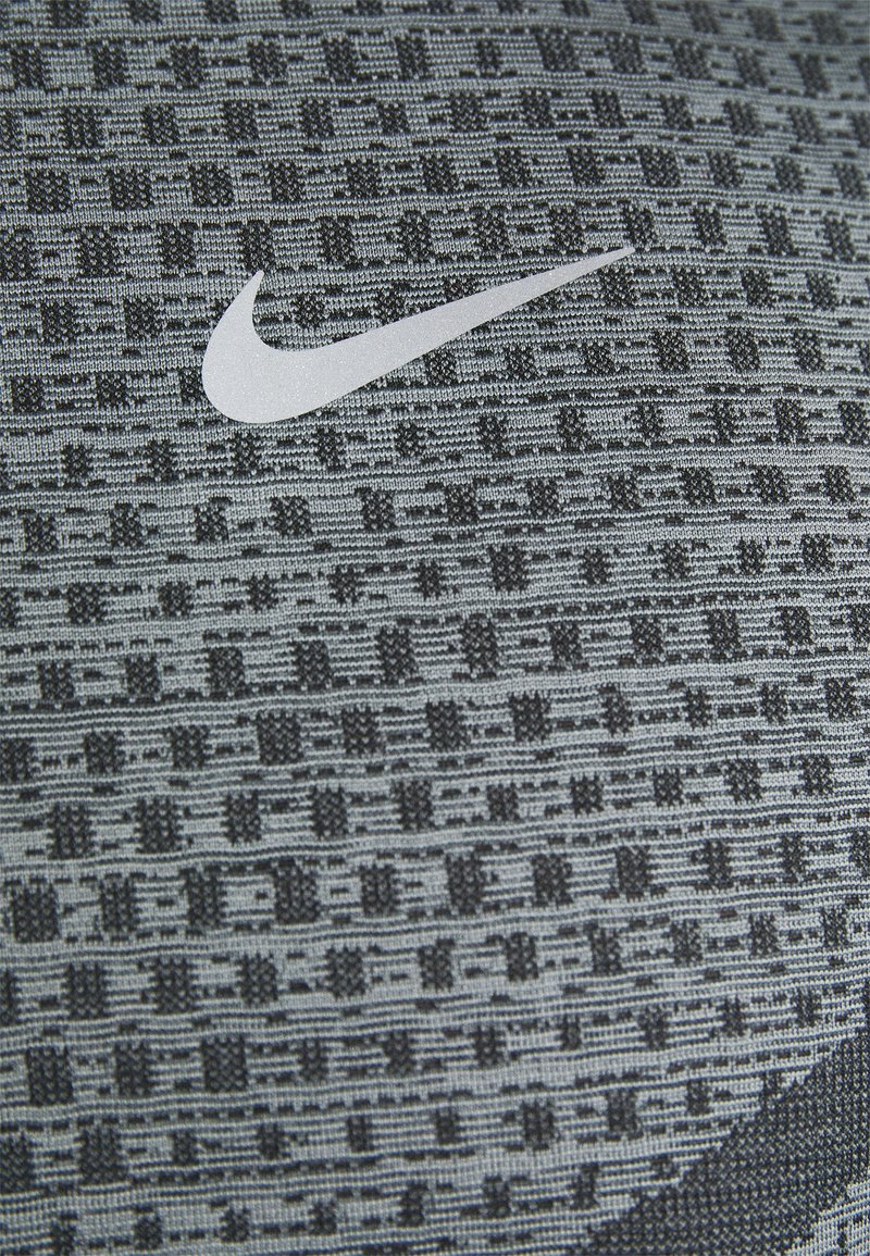 Der strukturierte Stoff von Nike in Grautönen weist ein texturiertes Muster mit einem auffälligen weißen Logo auf. Das Design umfasst geometrische Elemente.