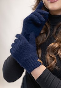 Námořnické pletené rukavice s vroubkovaným manžetou, s texturovaným povrchem a malou koženou značkou. Model má na sobě černé tričko.