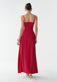 Vestido maxi rojo sin mangas con tirantes finos, cuerpo ajustado y falda fluida. Presenta una cremallera en la parte posterior y una tela suave y ligera.