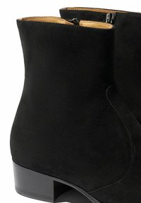 Botas de tobillo de ante negro con un tacón bajo en bloque, que cuentan con un cierre de cremallera en el lado y una textura suave y mate.