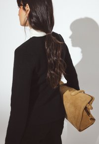 Must mustriga kootud sviiter pikkade varrukatega, kombinatsioonis beeži suede kotiga. Taust on valge, viskades varju pinnale.