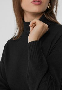 Schwarzer Rollkragenpullover mit gerippten Bündchen und Kragen, strukturiertem Strickstoff, der eine taillierte Form und ein minimalistisches Design zeigt.