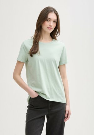 T-shirt in cotone organico verde chiaro con collo rotondo, maniche corte, vestibilità morbida, infilato in pantaloni di jeans scuri.