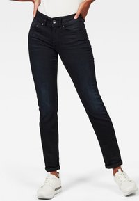 Svarta denimjeans med en figurnära design, som har hög midja, fem fickor och knappstängning. Matchas med vita sneakers.