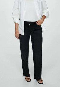 Black high-waisted jeans with a straight leg fit, frayed hem, and front pockets, paired with a white top and oversized white shirt.