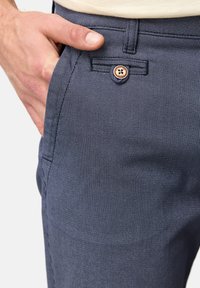 Pantalone mornarice plave boje s uzorkom izrađeni od lagane tkanine. Imaju vidljivo kopčanje na dugme i bočnu džep, s diskretnim teksturiranim dizajnom.