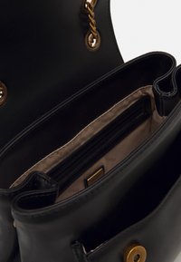 Černá kožená taška s detailem zlatého řetězu, vyznačující se hladkým povrchem, prostorným interiérem a kapsou na zip.