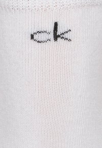 Gaiši rozā zeķes, izgatavotas no tekstūras adījuma, ar mazu melnu izšūtu "ck" logo tuvu augšai.