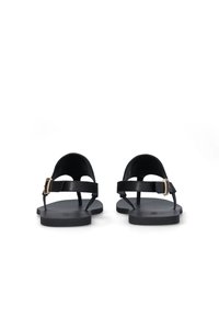 Sandales en cuir noir avec une semelle plate, dotées d'une bride à boucle et d'un design minimaliste. Texture lisse, dos ouvert et lignes simples.