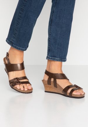 Brązowe sandały na koturnie z dwoma regulowanymi paskami, korkową podeszwą i gładką skórzaną teksturą. Otwarty przód odsłania bose stopy.