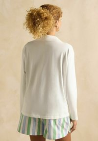 Valge pika varrukaga top, millel on sujuv tekstuur, koos roheliste ja siniste triibuliste lühikestega. Igapäevane riietus, vaadatuna selja tagant.