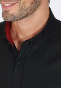 Chemise noire à boutons avec un col intérieur rouge, texture lisse et subtil éclat. Boutons noirs sur un design de col structuré.