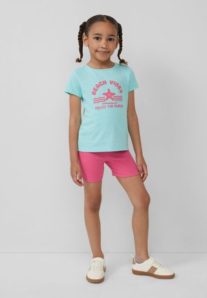 Lichtblauwe katoen T-shirt met roze tekst en sterafbeelding, gecombineerd met roze geribde shorts. Schoeisel: witte en tan sneakers.