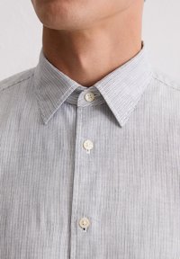 Koszula w paski w kolorze niebieskim i białym, z kołnierzykiem typu spread, małymi guzikami i miękką bawełnianą tkaniną. Widok z bliska.