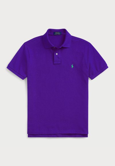 Polo shirt violet avec un logo brodé vert, manches courtes, col côtelé et patte de boutonnage à trois boutons. Tissu en coton doux.