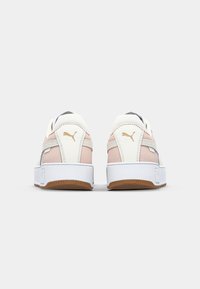 Pár růžových a bílých tenisek Puma zobrazených z zadní strany s bílou mezipodešví a hnědými gumovými podrážkami na bílém pozadí.