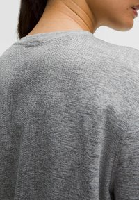 T-shirt in tessuto grigio con un motivo testurizzato, caratterizzato da una scollatura rotonda e maniche corte, visto da dietro con un dettaglio del logo vicino alla scollatura.