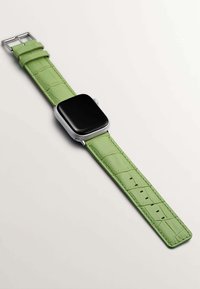 Correa de reloj de cuero verde con textura de cocodrilo, herrajes plateados y una esfera de reloj negra cuadrada posicionada en diagonal.