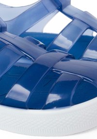 Blue transparent plastic sandals with crisscross design and a white rubber sole featuring textured grip patterns.