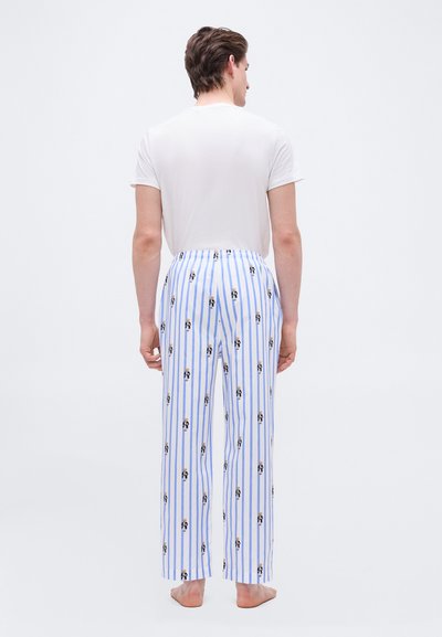 Ενήλικος άνδρας, γυμνόποδος, γυρισμένος με την πλάτη, φορώντας λευκή μπλούζα και ανοιχτό μπλε ριγέ πιτζάμα με μικρά σχέδια αρκούδας.