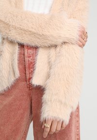 Light beige fuzzy cardigan with a soft texture, featuring long, slightly oversized sleeves. Paired with faded pink high-waisted jeans.