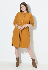 Senfgelbes, langärmliges Kleid mit einer Knopfkrause und seitlichen Schlitzen. Weicher Stoff mit lockerem Sitz, der vertikale Nahtdetails aufweist.