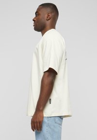 Cream-colored cotton t-shirt with short sleeves, round neckline, and side tag. The fabric has a soft, smooth texture, suitable for casual wear.
